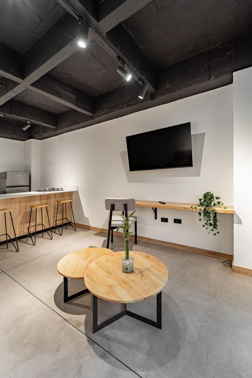 Zona social con smart TV en la pared, barra alta y mesas auxiliares de madera